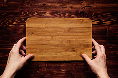 手握空白竹标志板在棕色复古木板上，俯视图。模拟公司身份，餐厅菜单，名片。图片下载