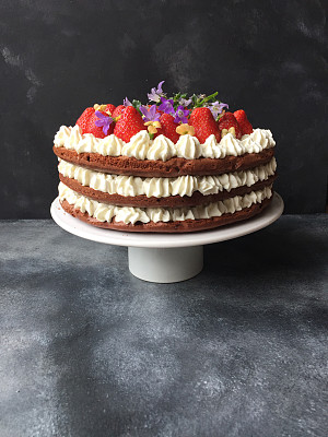 三层巧克力蛋糕，奶油，草莓和花在蛋糕基座上图片下载