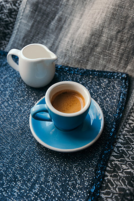 美味的早晨新鲜煮的浓缩咖啡与美丽的老虎crema，小牛奶罐的背景。照片是蓝色的:蓝色的杯子，蓝色的茶碟，蓝色的餐巾图片下载