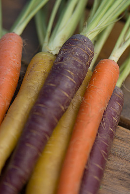 红色，橙色，黄色和紫色的胡萝卜和叶子在木桌上图片下载