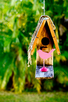 简单质朴的木制鸟笼，以绿色植物为背景，配以粉红色的鸟形图案图片下载