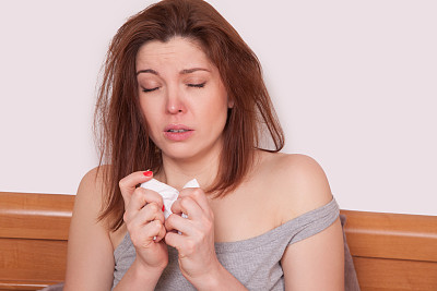 一个红鼻子的生病妇女坐在床上。打喷嚏图片下载