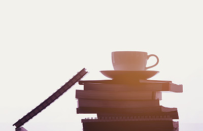 咖啡杯上堆叠的书籍，剪影风格与光晕。图片下载