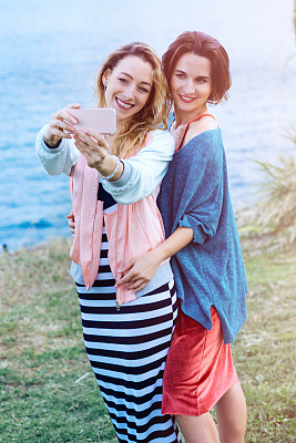 两个漂亮的女人或学生用智能手机自拍图片下载