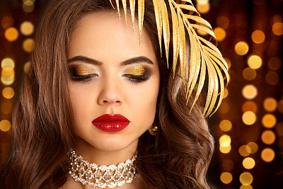 美丽的金色眼妆。时尚的黑发肖像在黄金。性感优雅的女人，红唇，闪闪发光的眼影在昂贵的钻石项链在圣诞灯光的背景。图片下载