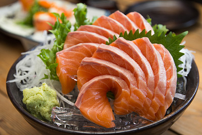 特写拍摄的日本鲑鱼生鱼片在黑色的碗在木制的背景。图片下载