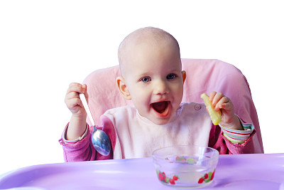 微笑的小女孩坐在婴儿椅上吃着柠檬，孤立的白色背景图片下载