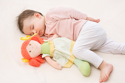 可爱和美丽的婴儿学步与一个橙色头发的娃娃睡觉。图片下载