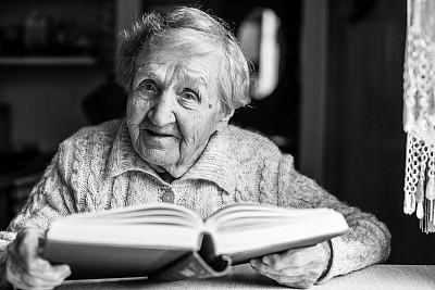 一位老太太坐在桌子旁看书。黑白照片。图片下载