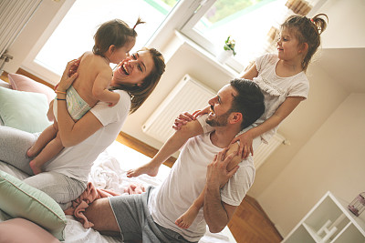 家人在家里度过空闲时间。欢乐的家庭和他们的女儿在床上玩得很开心。图片下载