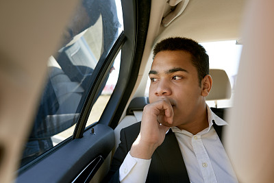 一个穿着西装的年轻人坐在汽车的后座上图片下载