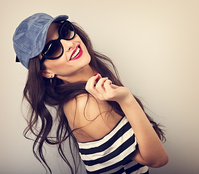 享受年轻女子在太阳镜和蓝色棒球帽摆姿势和看着条纹衬衫微笑。特写肖像快乐。缓和的肖像图片下载