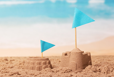 沙滩城堡，斗兽场和蓝色旗帜的背景海岸。图片下载