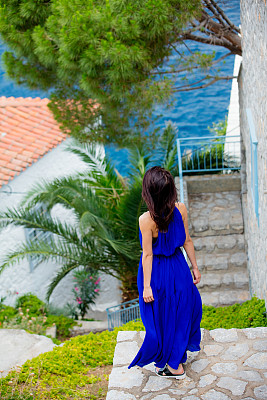 一张美丽的年轻女子站在房子附近的楼梯上，看着希腊的大海的照片图片下载