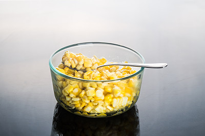 玉米粒置于透明的玻璃碗中，背面呈深色反光图片下载