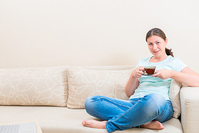 坐在沙发上，端着一杯茶的女人图片下载