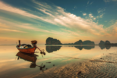 倒影在沙滩上的长尾船越过五彩缤纷的天空素材图片