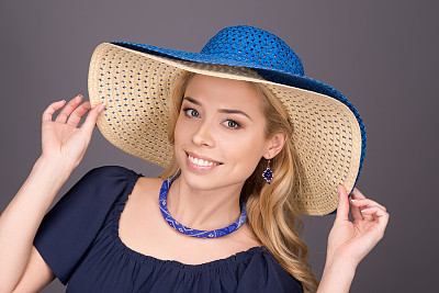 年轻女子在灰色背景的蓝色太阳帽微笑图片下载