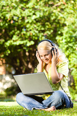 年轻女子在户外用笔记本电脑听音乐图片下载