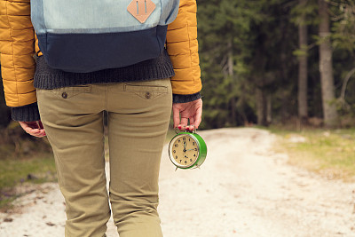 在一条空荡荡的泥土路上，一个女孩拿着一个古董钟。图片下载