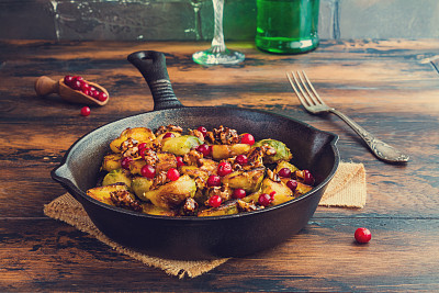 烤球芽甘蓝，焦糖核桃和蔓越莓在一个铸铁煎锅，在木桌上。图片下载