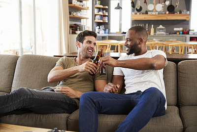 两个男性朋友坐在沙发上看电视上的体育节目图片下载