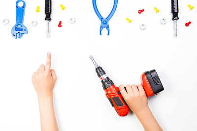 孩子手持钻子，手指指向白色背景上的玩具工具。图片下载