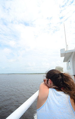 一个十几岁的女孩，胳膊搭在船栏杆上，向外看图片下载