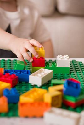 近距离的孩子的手玩彩色塑料砖在桌子上。蹒跚学步的孩子有乐趣和建筑明亮的构造砖。早期的学习。条纹背景。开发的玩具图片下载