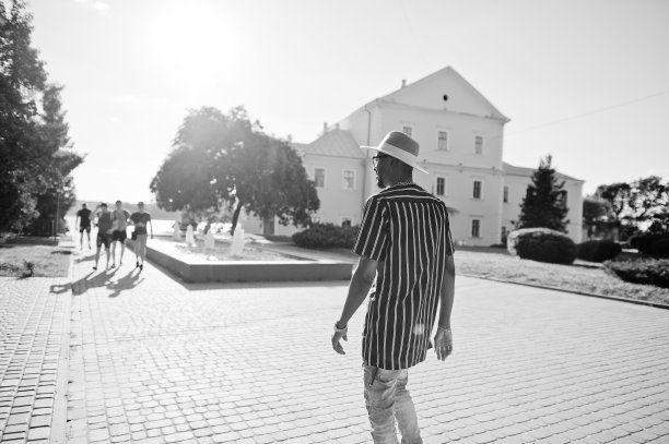 迷人的非裔美国人穿着条纹衬衫，帽子和太阳镜走在市中心的街道上。黑白照片。图片下载