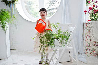 漂亮的小女孩穿着裙子给植物浇水。图片下载