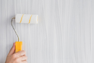 一个男人的手用油漆滚轴把一个旧木板漆成白色，它看起来像一个新的。更新旧事物。图片下载