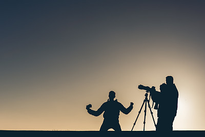 夕阳下三个摄影师的剪影，一个在庆祝。图片下载