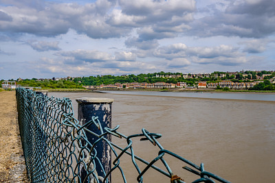 铁丝围栏的近景，看到邻近的一个大河岸的步道。图片下载
