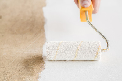 一个男人的手用油漆滚轴把一个旧木板漆成白色，它看起来像一个新的。更新旧事物。图片下载