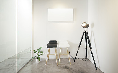 空的办公室等候室，玻璃窗户与绿色植物的左边，复古摄影站灯的右边。阁楼的室内风格，白色帆布打印在中央白墙。水泥地上放着两把黑白相间的椅子。图片下载