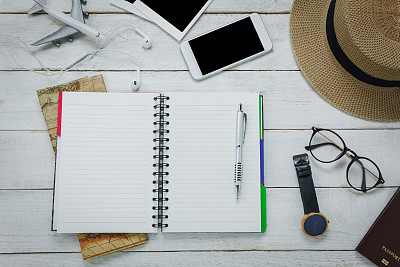 俯视图配件旅行概念。笔记本的空白空间，书写与钢笔在白色的背景。物品是地图,手表,眼镜,护照,帽子,手机,飞机,眼机、照片。图片下载