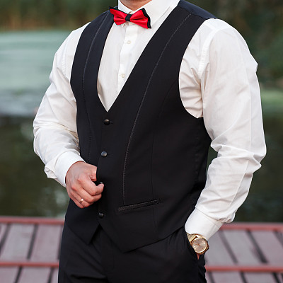 年轻时尚的男子穿着马甲，竖着画像的新郎，画像的背景是自然、河流和码头，看着相机，手里拿着金表。经营理念。图片下载