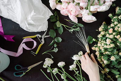 花店工作间，平铺。新鲜的小玫瑰，粉红色的毛茛，包装纸，剪刀放在深色的木桌背景上图片下载