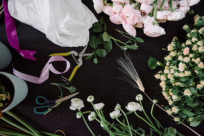 花店工作间，平铺。新鲜的小玫瑰，粉红色的毛茛，包装纸，剪刀放在深色的木桌背景上图片下载