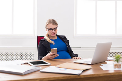 年轻孕妇在办公室使用智能手机图片下载