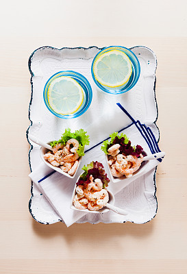 在木桌上的心形碗里盛着鸡尾虾。放在一个白色的节日托盘上。两杯水加冰图片下载