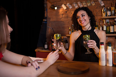 漂亮微笑的女调酒师为站在吧台后面的客人提供饮料素材图片