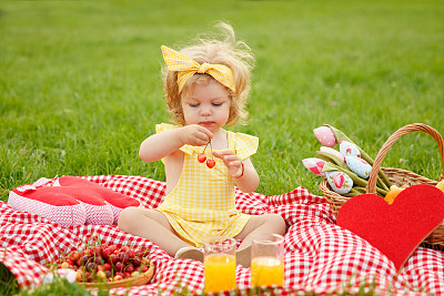 小女孩拿着樱桃坐在毯子上图片下载