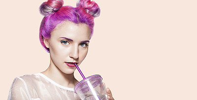 一名身穿白色连衣裙、头发五彩缤纷的年轻女子用吸管从一个漂亮的彩色玻璃杯里喝着酒素材图片