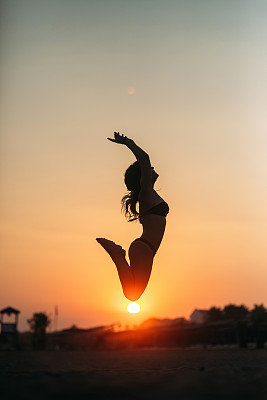 在沙滩上晒太阳的漂亮女孩。日落轮廓图片下载