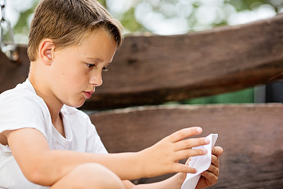 一个白人男孩在学习折纸船图片下载
