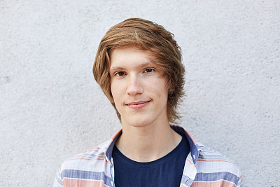 近距离的英俊的男性与黑眼睛，纯健康的皮肤和薄嘴唇直视镜头与严肃的表情。嬉皮士男孩与迷人的外表，摆姿势靠白墙图片下载