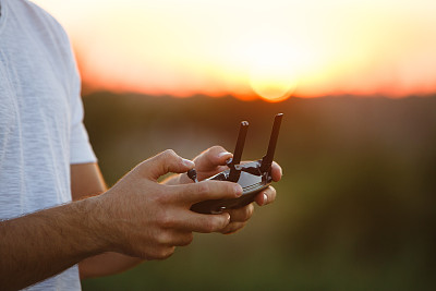 一名男子手里拿着一个无人机遥控器。近距离的四旋翼机遥控飞行。飞行员在日落时用飞机拍摄照片和视频图片下载