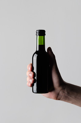 葡萄酒季/迷你酒瓶模型-男性的手拿着一个酒瓶在灰色的背景图片下载